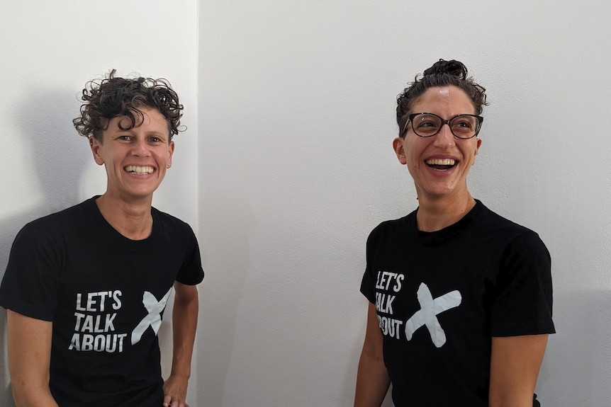 Two people with short dark hair smiling. They are both wearing dark T-shirts that says Let's Talk About X.'s Talk About X.